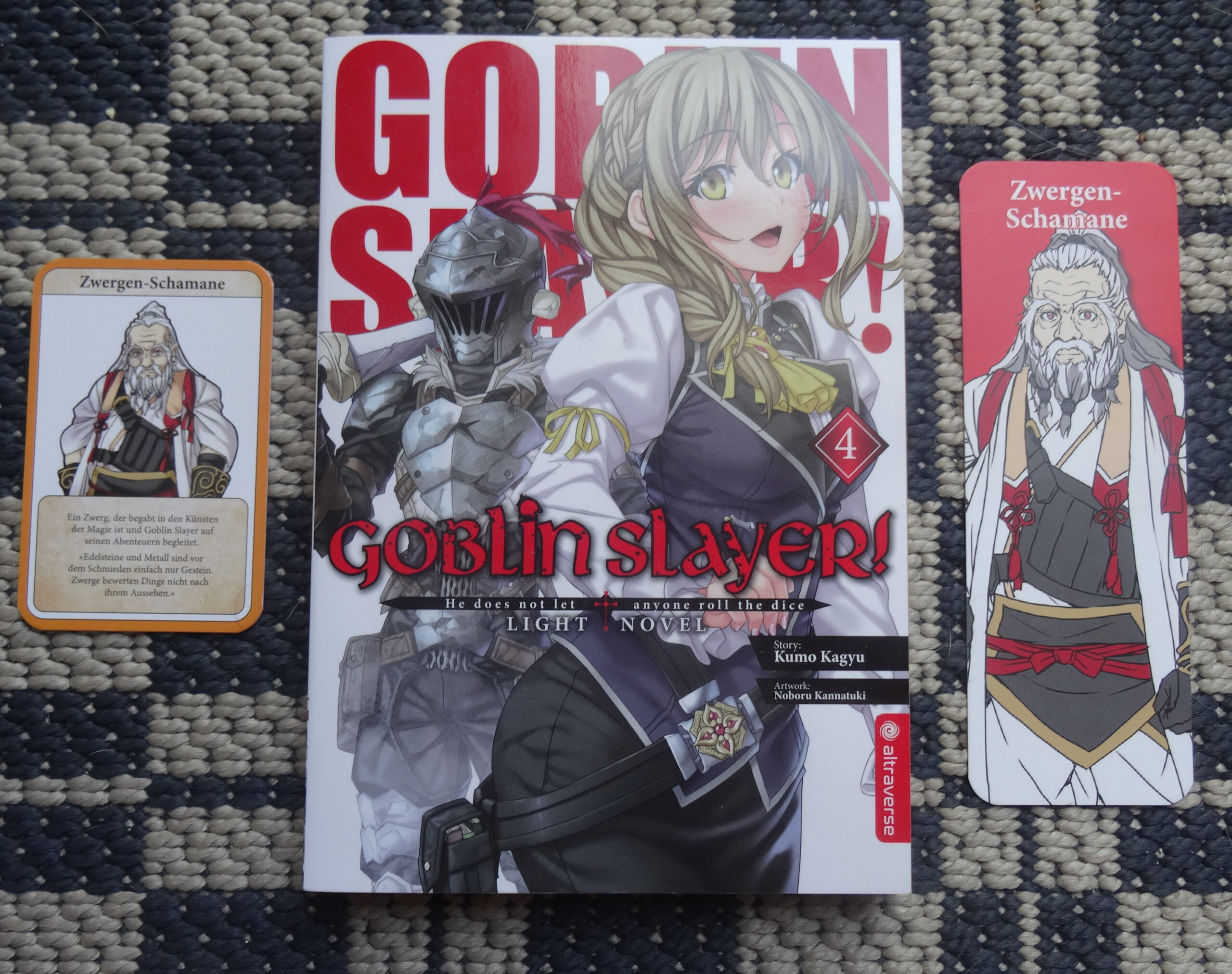 Band 4 der Goblin Slayer Light Novel mit allen Extras. Auf der linken Seite die Charakterkarte des Zwergen-Schamanen und auf der rechten Seite das passende Lesezeichen.