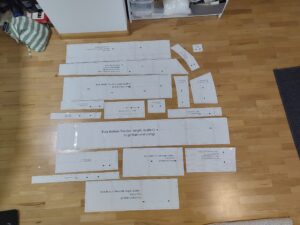 all the pattern-pieces cut out of paper and laid out on the floor. The skirt pieces are mostly rectangles, the shirring panel is a trapezoid. there is also long wait-ties and all the pieces for the (wrong bodice)